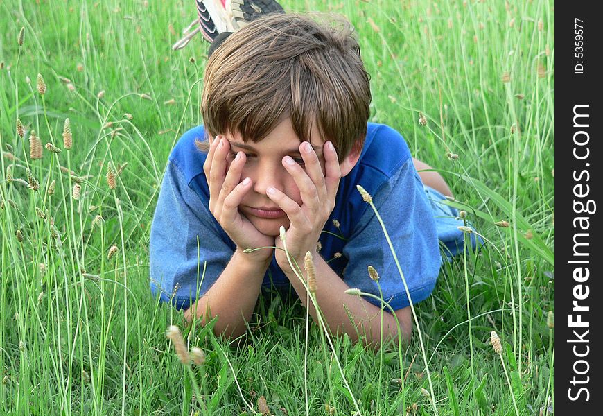 Boy in blue t-shirt with hands over eyes; he is lying in the grass/field. Boy in blue t-shirt with hands over eyes; he is lying in the grass/field