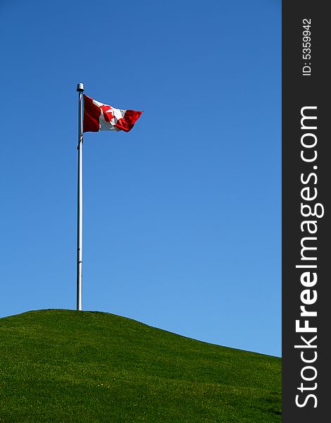 Canadian flag flying over a grassy hill under a blue sky