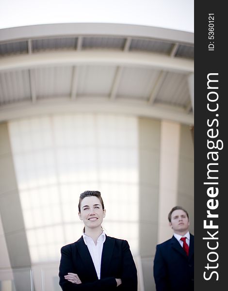 Front view of young businesswoman standing with arms crossed and businessman standing behind her