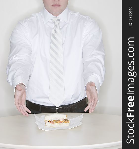 A businessman stands at the front of a table showing a new sandwich. A businessman stands at the front of a table showing a new sandwich