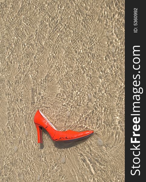 A red and pink stiletto shoe in ocean water. A red and pink stiletto shoe in ocean water