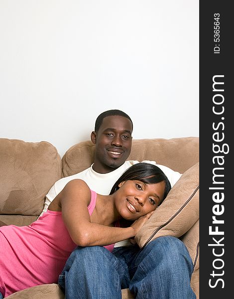 Attractive smiling young couple relaxing on a sofa.  The man is sitting, and the woman lying with her head in his lap.  Vertically  framed shot with copy-space above the sofa. Attractive smiling young couple relaxing on a sofa.  The man is sitting, and the woman lying with her head in his lap.  Vertically  framed shot with copy-space above the sofa.