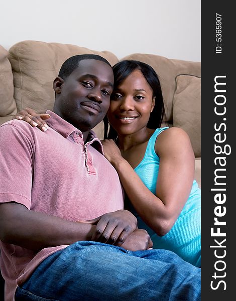 A young couple sitting together by a sofa smiling. A young couple sitting together by a sofa smiling.