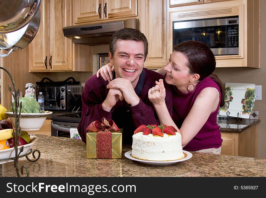 Attractive, playful couple laughing together in their kitchen over gifts and cake. Attractive, playful couple laughing together in their kitchen over gifts and cake.