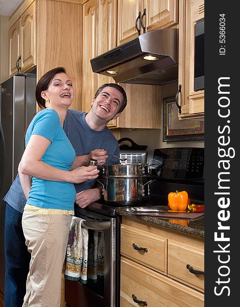 Attractive couple stand in the kitchen by the stove laughing heartily while looking at the camera. Vertically framed shot. Attractive couple stand in the kitchen by the stove laughing heartily while looking at the camera. Vertically framed shot.