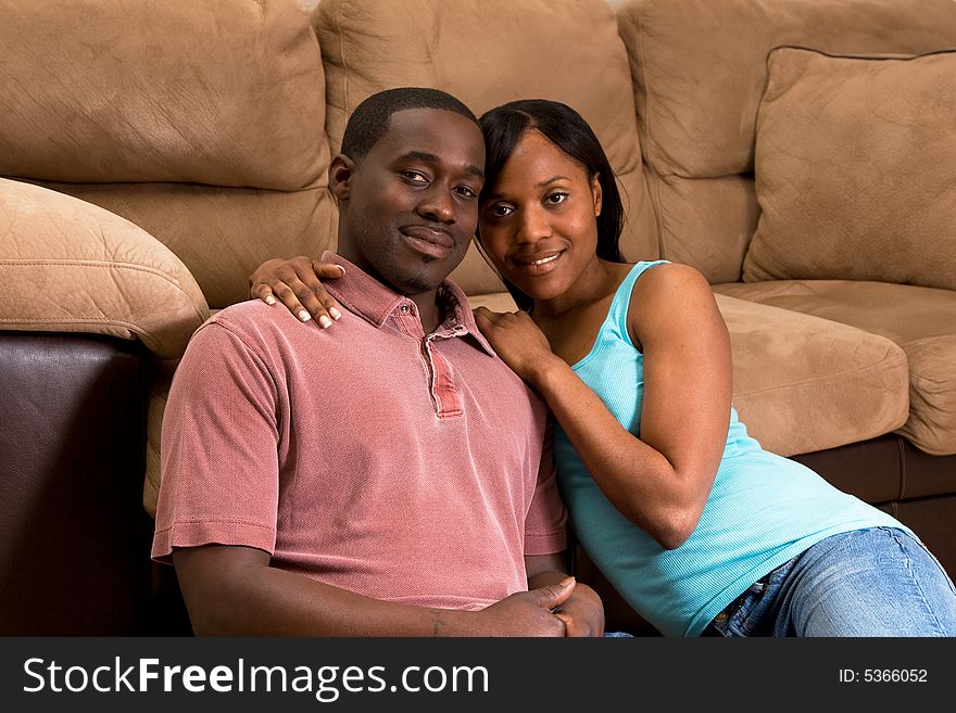 A young couple sitting together on the floor by a sofa. Horizontally framed shot. A young couple sitting together on the floor by a sofa. Horizontally framed shot.