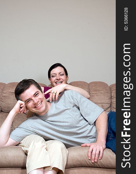 Couple horsing around on their living room couch. He is lying in her lap and she is tickling his ear. Both are laughing at the camera. Vertically framed shot. Couple horsing around on their living room couch. He is lying in her lap and she is tickling his ear. Both are laughing at the camera. Vertically framed shot.