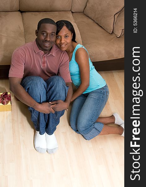 A young smiling couple sitting on the floor by a gift box in front of a sofa. A young smiling couple sitting on the floor by a gift box in front of a sofa.