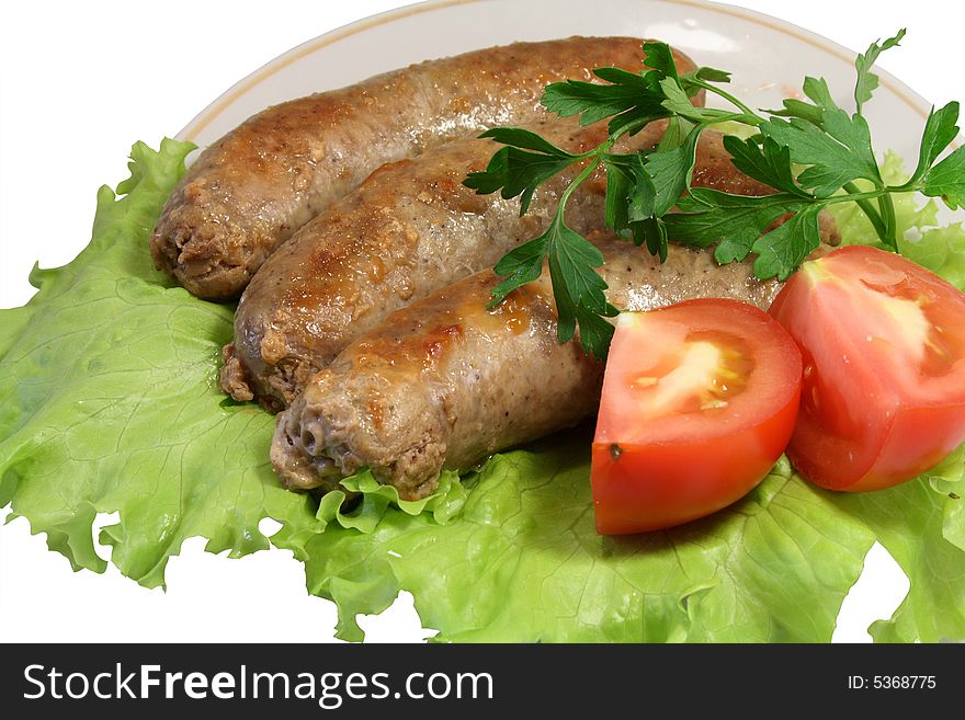 Three fried sausages on leaves of green salad with slices a tomato and a parsley.