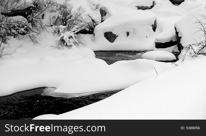 Snow drifts create unusual shapes over the boulders of a mountain river in Colorado. Snow drifts create unusual shapes over the boulders of a mountain river in Colorado.