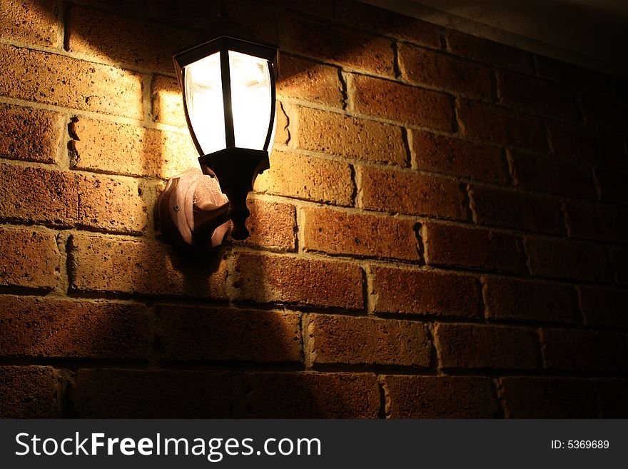 An electrical lamp attached to a brick wall shining at night. An electrical lamp attached to a brick wall shining at night
