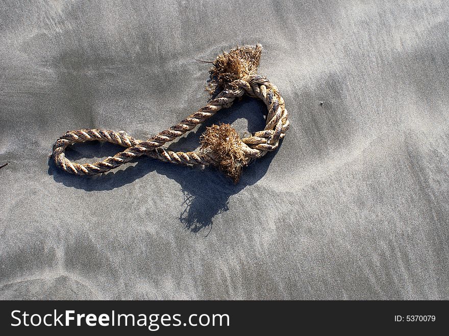 A old brown rope staying on the grain beach with sand.