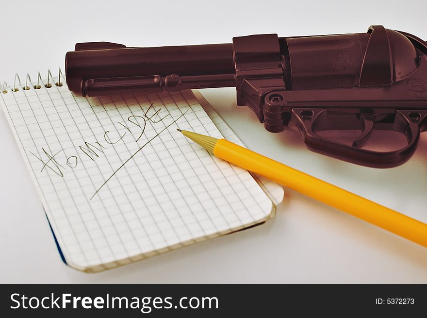 Close-up of a notepad with word 'homicide' written with pencil and gun with selective focus