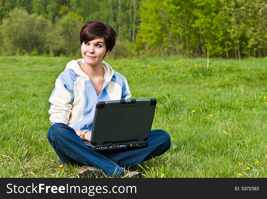 Young attractive girl sits on a green grass with a portable computer. Young attractive girl sits on a green grass with a portable computer