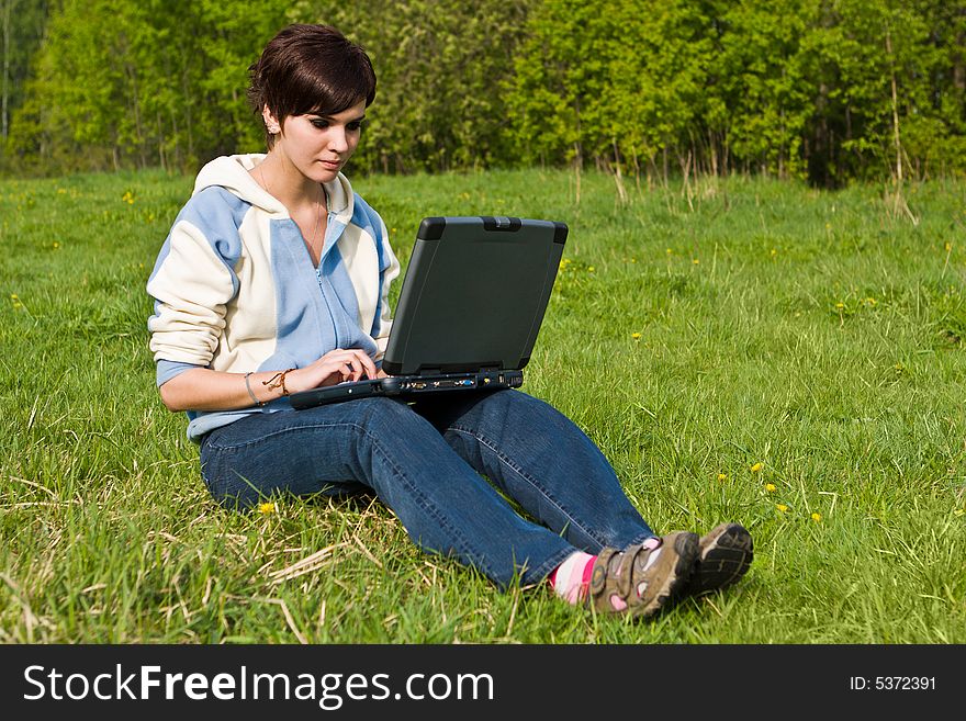 Young attractive girl sits on a green grass with a portable computer. Young attractive girl sits on a green grass with a portable computer