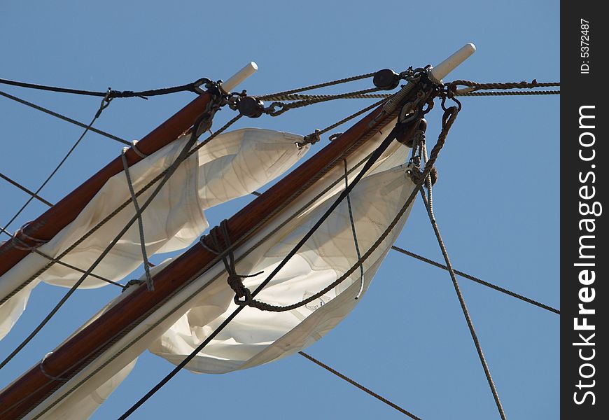 2 yards with sails partly unwounded of a sailing boat against a blue sky. 2 yards with sails partly unwounded of a sailing boat against a blue sky