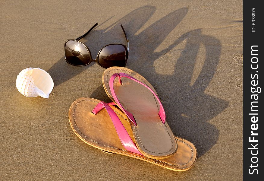 Close up of slippers, sunglasses and shell on sand background. Close up of slippers, sunglasses and shell on sand background