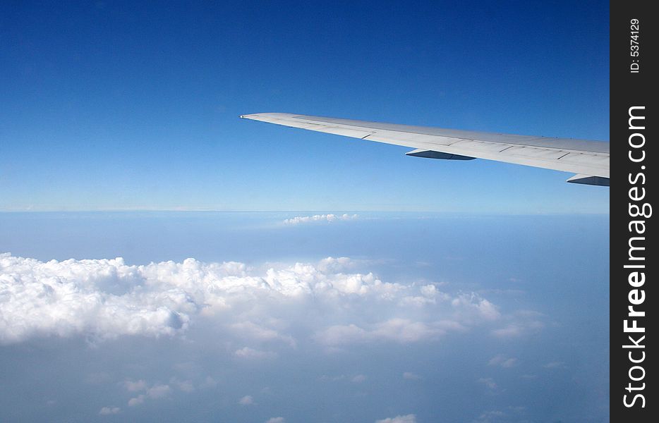 An airplane wing is seen from the window of a jet and is overlooking the clouds.