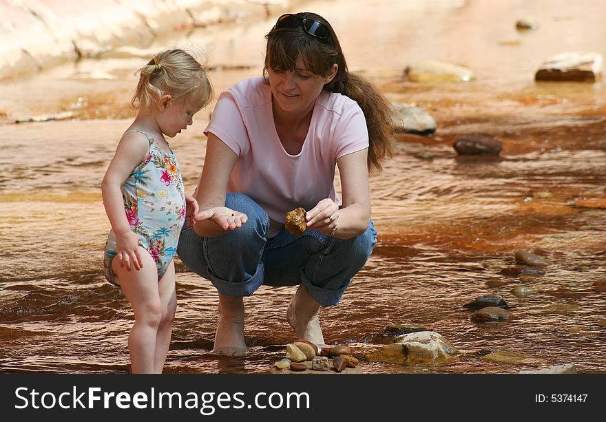 A Woman Shows a Toddler an Interesting Rock While Wading in a Shallow Creek. A Woman Shows a Toddler an Interesting Rock While Wading in a Shallow Creek