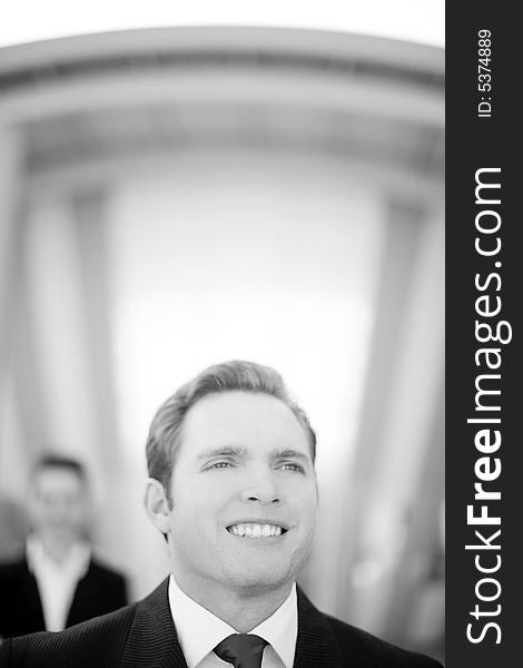 Front view of young businessman standing wearing suit with businesswoman standing behind him. Front view of young businessman standing wearing suit with businesswoman standing behind him