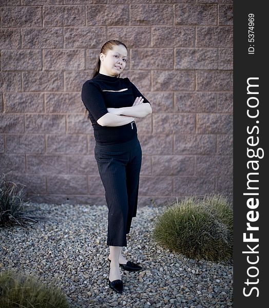 Young Asian Woman standing outside against a brick wall with her arms crossed while wearing a black business outfit