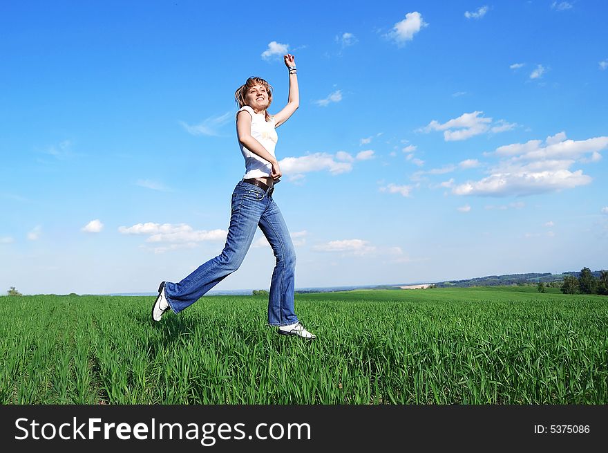 Young active woman running at the green field at the blue sky background. Young active woman running at the green field at the blue sky background