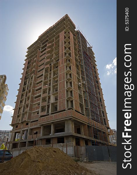 A towering building under construction against blue sky; the sun is behind the building