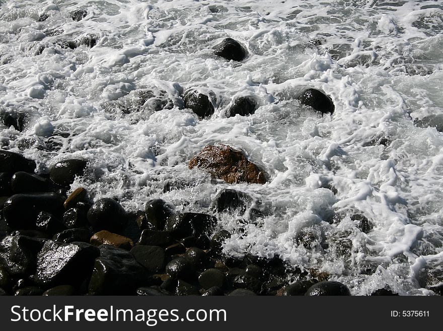 Sea Water streaming in over black wet pebbles