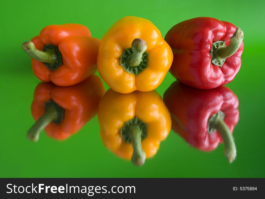 Red, orange and yellow paprika on the green background. Red, orange and yellow paprika on the green background