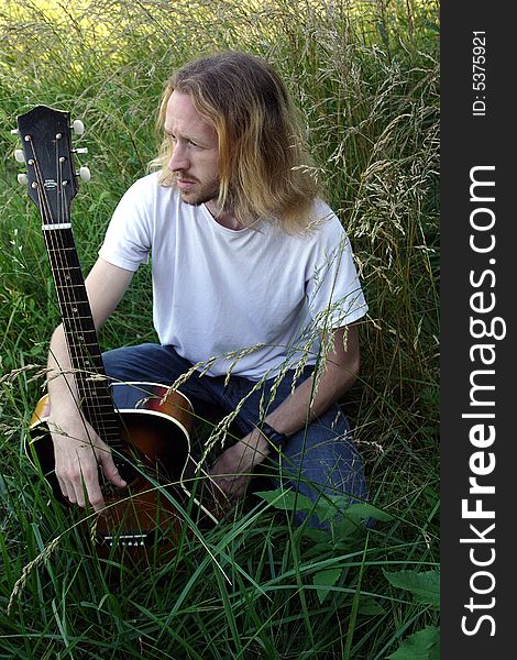 A guitar player poses in the tall grass. A guitar player poses in the tall grass.