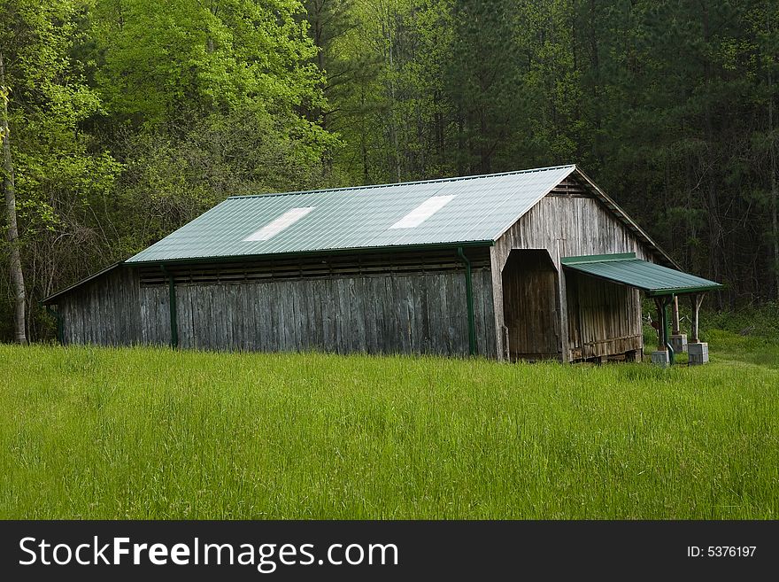Side view of a weathered old pole barn, with green, roof, in a pasture, in front of a forest. Side view of a weathered old pole barn, with green, roof, in a pasture, in front of a forest.