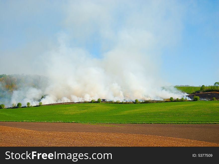 Field on fire with green pasture and blue sky. Field on fire with green pasture and blue sky