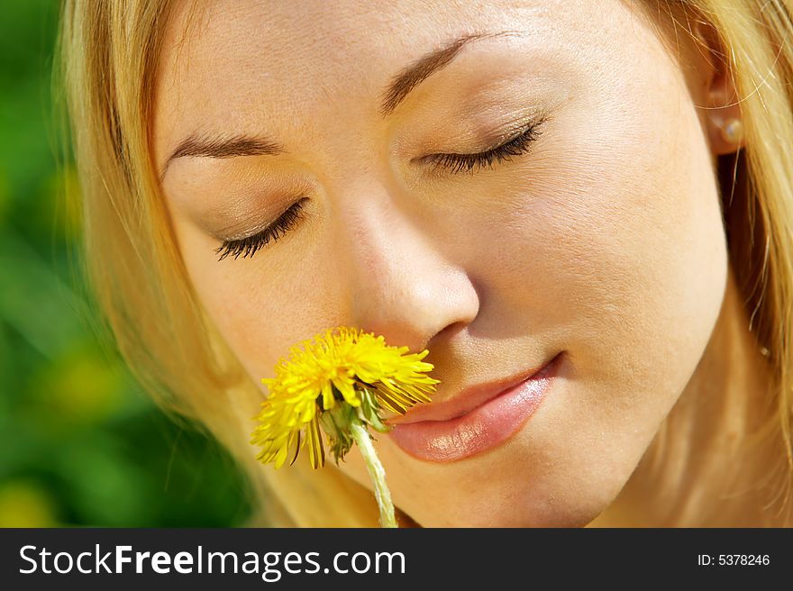 The beautiful girl enjoys aroma of a yellow flower. The beautiful girl enjoys aroma of a yellow flower