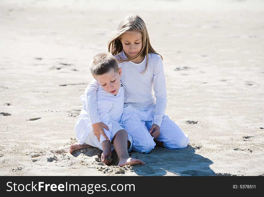 Portrait of blond sister and brother sitting in the sand dressed in white in summertime. Portrait of blond sister and brother sitting in the sand dressed in white in summertime