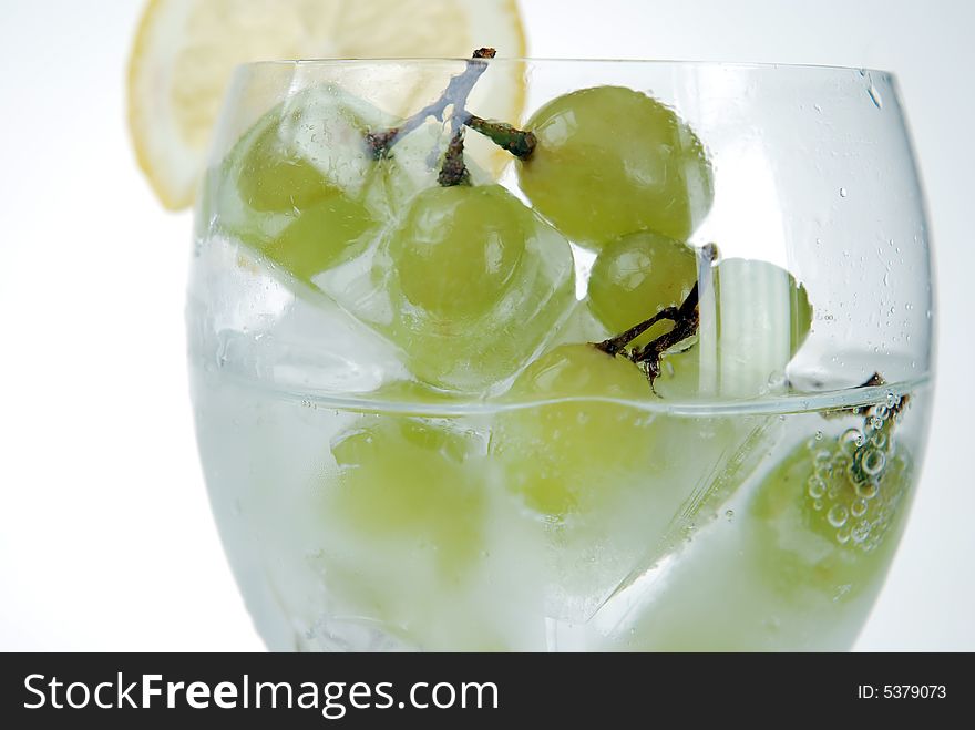 Close up to frozen grapes in wine glass filled with soda serving with fresh cut lemon slice. Close up to frozen grapes in wine glass filled with soda serving with fresh cut lemon slice
