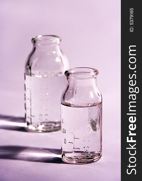 Two glass  measure bottles on violet background. Two glass  measure bottles on violet background