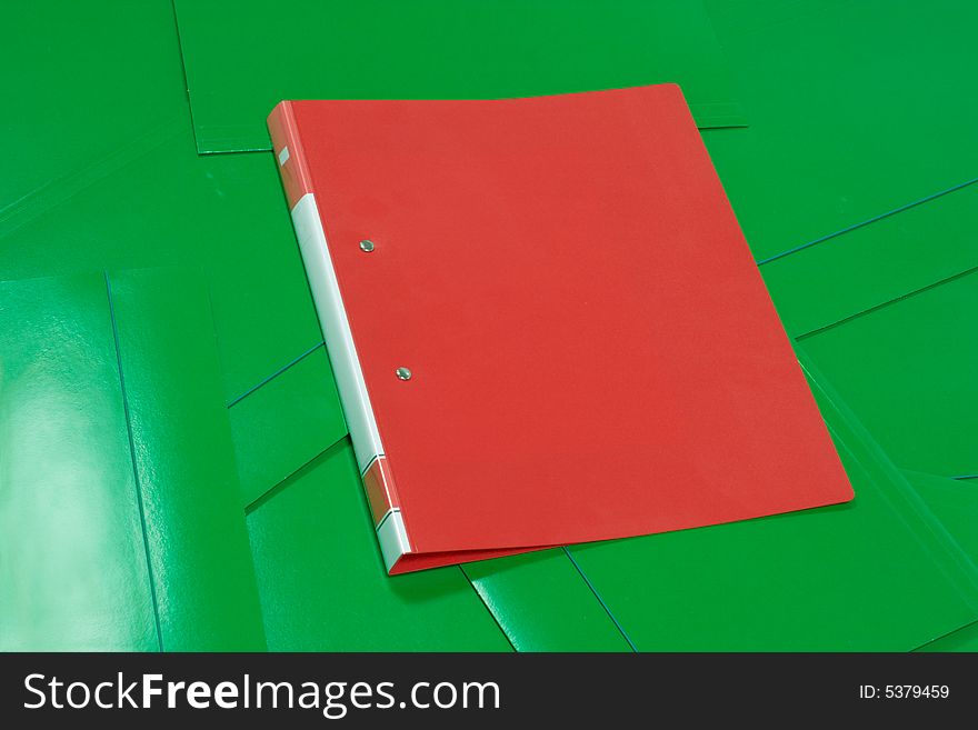 A single red folder, lying on a heap of green folders