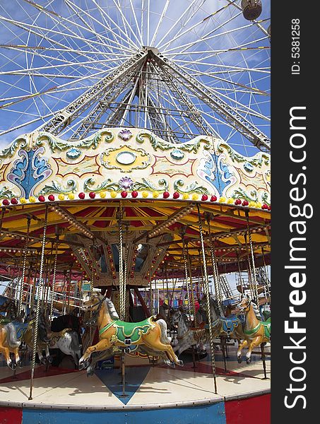 Fairground carousel ride with horses on seaside pier with big wheel in background. Fairground carousel ride with horses on seaside pier with big wheel in background