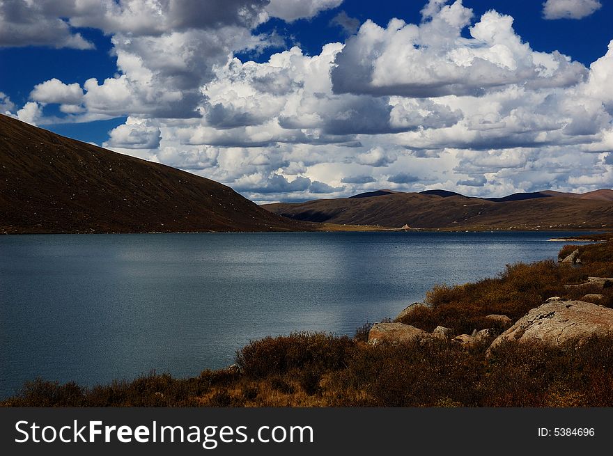When travelling in Tibet of China, a  beautiful lake on field appears in front of us, with a lot of clouds in the sky.