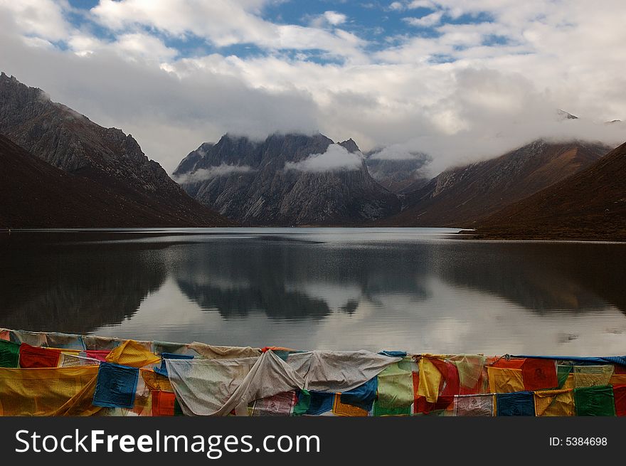 When travelling in Tibet of China in a morning, a beautiful lake with some mist beside mountains appears in front of us, and there are many Tibet flags around the lake. When travelling in Tibet of China in a morning, a beautiful lake with some mist beside mountains appears in front of us, and there are many Tibet flags around the lake.