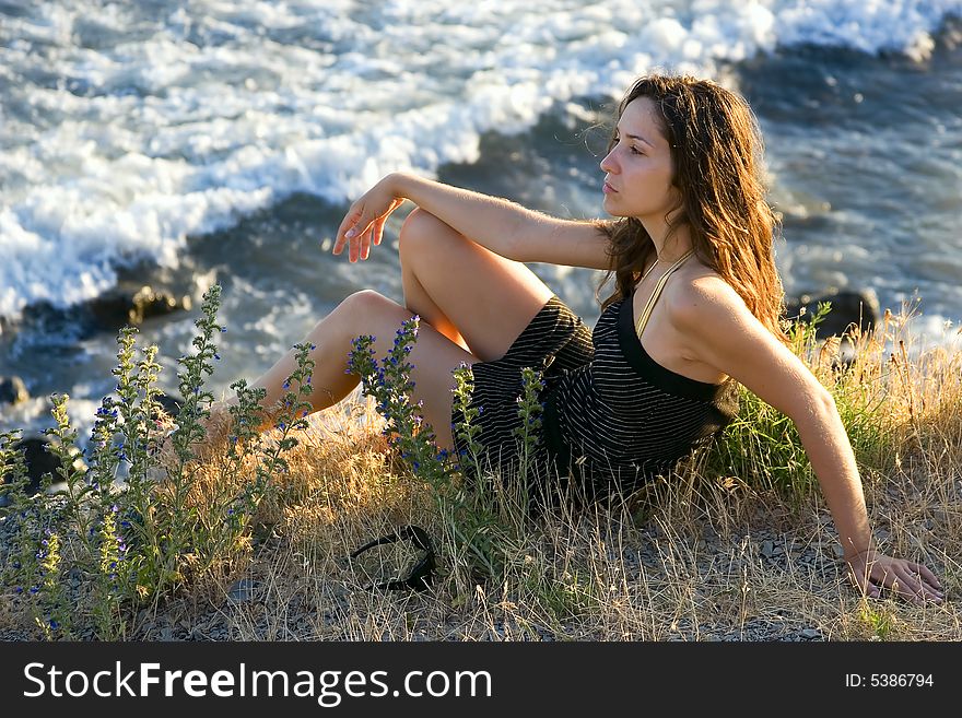 Pretty young woman sitting on the grass beside the sea. Pretty young woman sitting on the grass beside the sea