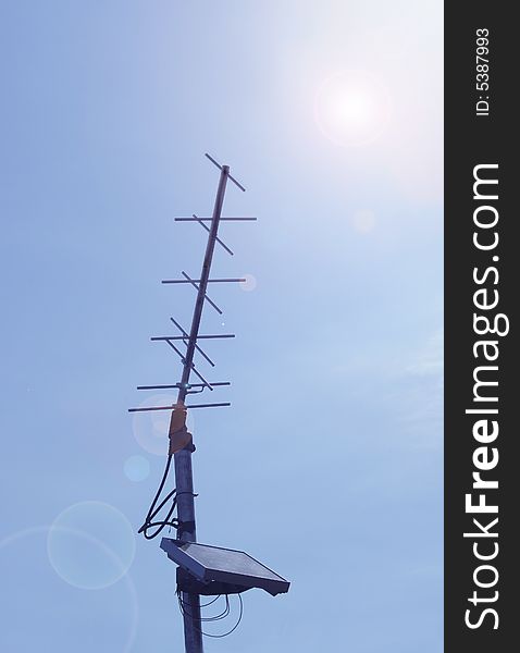 An antenna with solar power device on blue sky background with a sun glare. An antenna with solar power device on blue sky background with a sun glare