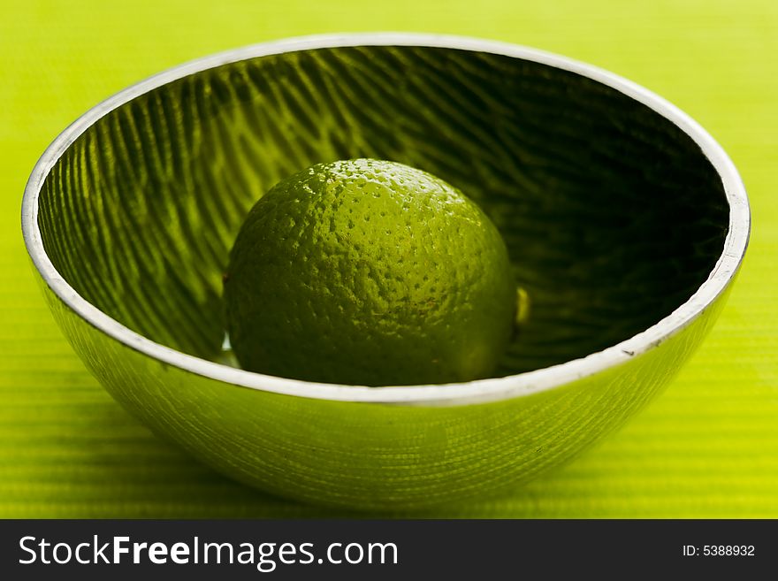 One lime on the small metal bowl over green background