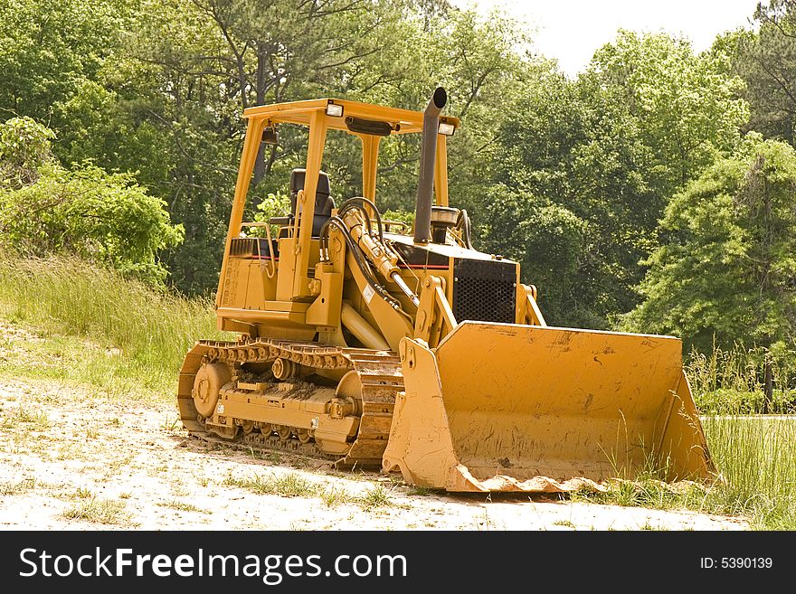 An orange bulldozer in a field by the trees. An orange bulldozer in a field by the trees