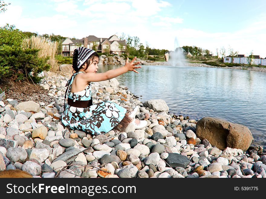 Two year old girl dressed up by the lake throwing rocks