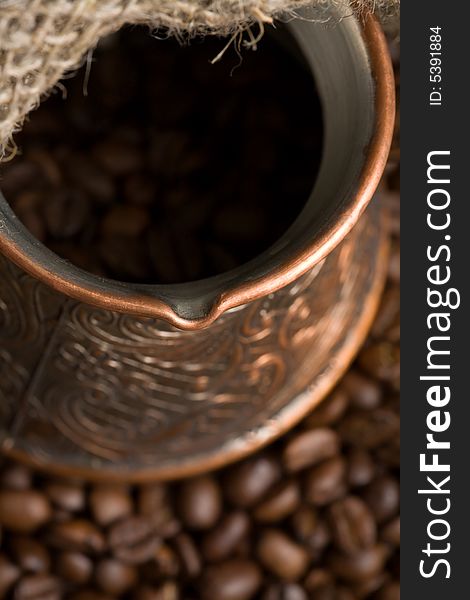 Cezve with freshly roasted coffee beans on sackcloth. Shallow depth of field. Focus on cezve throat