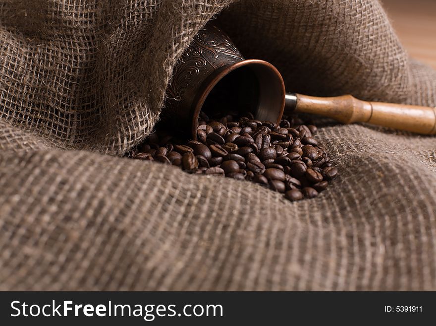 Cezve with freshly roasted coffee beans on sackcloth. Shallow depth of field. Focus on center of image