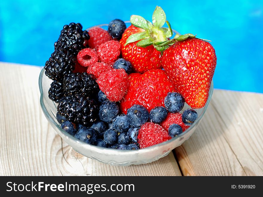 Bowl of mixed berries on a wooden deck near a pool. Bowl of mixed berries on a wooden deck near a pool