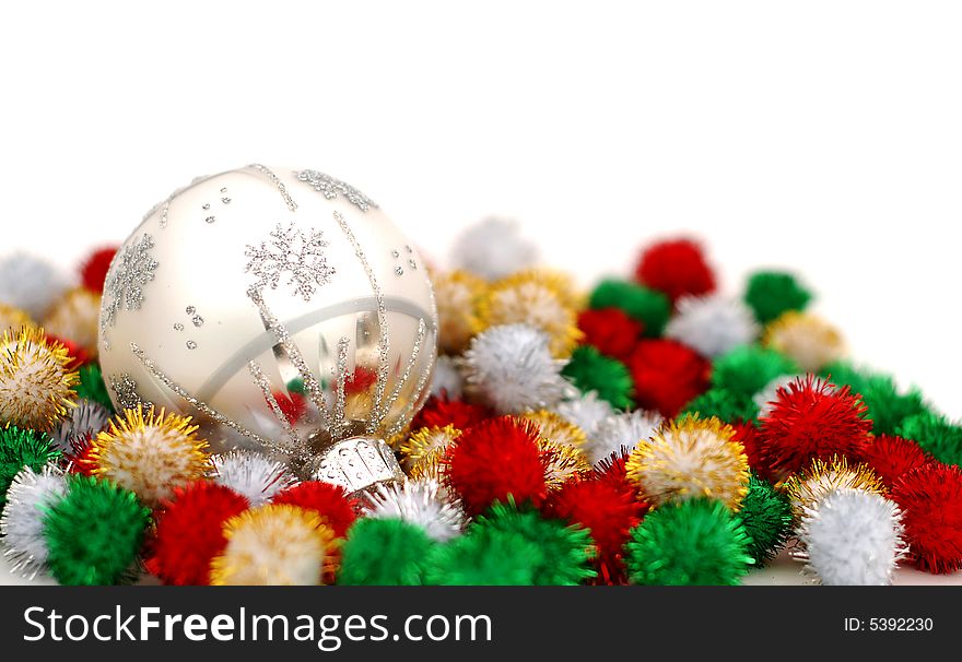 Silver Christmas bauble resting on colorful puff ball decoration over a white background. Silver Christmas bauble resting on colorful puff ball decoration over a white background