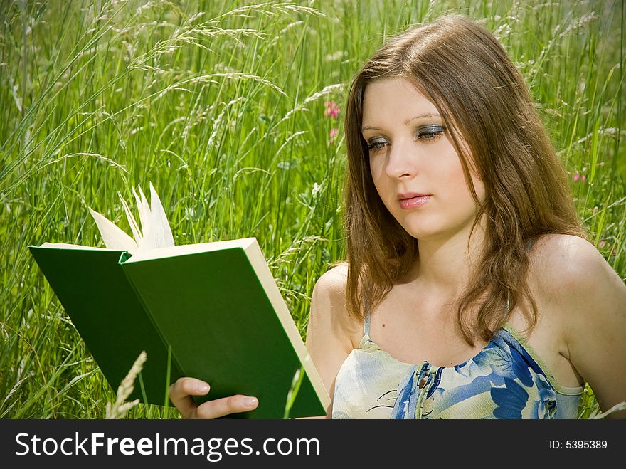 Cute young romantic girl reading an interesting book, sitting in tall grass. Cute young romantic girl reading an interesting book, sitting in tall grass